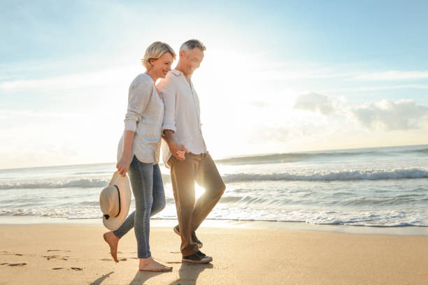 Relaxed mature couple walking together on a calm beach with soft ocean light